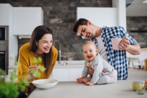 Happy Family With Mom And Dad Feeding Baby On Kitchen Countertop